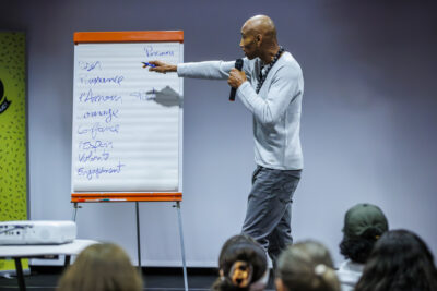 Aurelien Duarte sur la scène du Virtuoz Club de Villeneuve-la-Garenne tient dans sa main un micro pour présenter sa conférence. - Agrandir l'image 3 sur 6, fenêtre modale