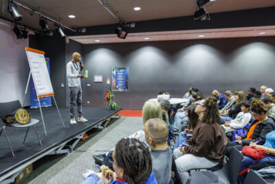 Aurelien Duarte sur la scène du Virtuoz Club de Villeneuve-la-Garenne tient dans sa main un micro pour présenter sa conférence. - Agrandir l'image 2 sur 6, fenêtre modale