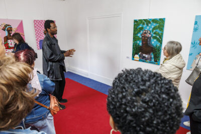 Plusieurs personnes regardent les tableaux de l'artiste Jules Be Kuti avec une explication de celui-ci, lors du vernissage de l'exposition qui lui est consacré à Villeneuve-la-Garenne. - Agrandir l'image 4 sur 6, fenêtre modale