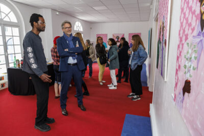 Plusieurs personnes regardent les tableaux de l'artiste Jules Be Kuti avec une explication de celui-ci, lors du vernissage de l'exposition qui lui est consacré à Villeneuve-la-Garenne. - Agrandir l'image 5 sur 6, fenêtre modale