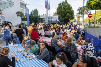 Plusieurs habitants sont réunis sur les tables et dégustent les différents plats des food trucks dans le cadre de la soirée food trucks et musique de Villeneuve-la-Garenne. - Agrandir l'image 2 sur 6, fenêtre modale