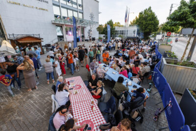 Plusieurs habitants sont réunis sur les tables et dégustent les différents plats des food trucks dans le cadre de la soirée food trucks et musique de Villeneuve-la-Garenne. - Agrandir l'image 5 sur 6, fenêtre modale