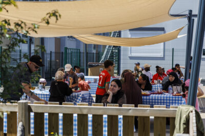Des familles sont assises sur des tables à la fête des accueils de loisirs de Villeneuve-la-Garenne - Agrandir l'image 3 sur 6, fenêtre modale
