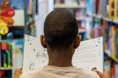 On voit le dos de la tête d'un enfant qui est en train de lire un livre dans une bibliothèque. - Agrandir l'image, fenêtre modale
