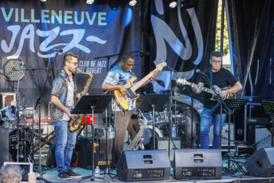 Trois hommes jouent de la guitare et du saxophone sur la scène du Villeneuve Jazz de Villeneuve-la-Garenne - Agrandir l'image 2 sur 6, fenêtre modale