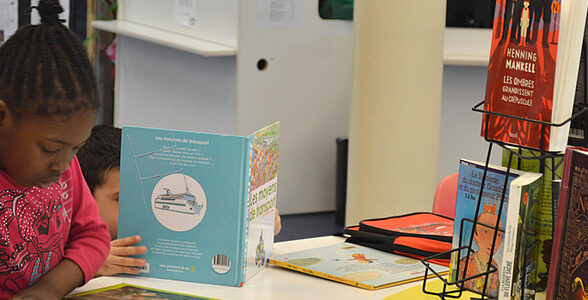 enfant avec un tee shirt rose en train de lire à la bibliotheque