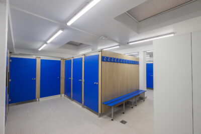 Des cabines de vestiaire individuelles bleues, alignées avec des bancs devant. - Agrandir l'image 3 sur 7, fenêtre modale