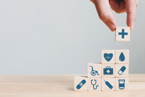 photo avec des petits cubes tenu par une main qui représentent des symboles de la santé (cœur, croix de pharmacie)