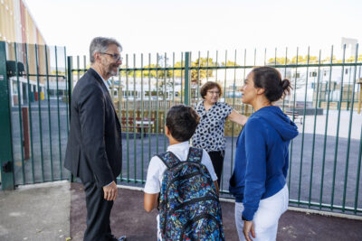 Monsieur le Maire parle avec une maman et son fils devant une école - Agrandir l'image 1 sur 6, fenêtre modale