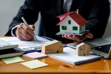 Un homme tient une maquette d'une petite maison et écrit sur une feuille sur son bureau