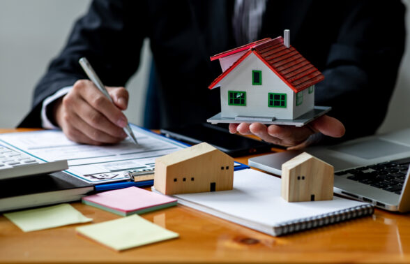 Un homme tient une maquette d'une petite maison et écrit sur une feuille sur son bureau