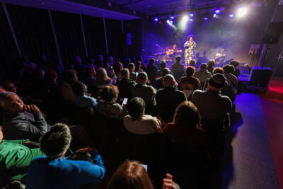 spectateurs du concert de Lucibela et en fond Lucibela en train de chanter sur scène - Agrandir l'image 4 sur 6, fenêtre modale