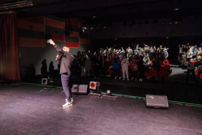L'humoriste Kosh tenant son téléphone pour faire un selfie avec les spectateurs - Agrandir l'image 5 sur 6, fenêtre modale