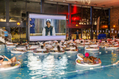 Plusieurs personnes sont assis dans une bouée gonflable à la piscine municipale de Villeneuve-la-Garenne face à un écran géant pour regarder un film à l'événement ciné piscine - Agrandir l'image 6 sur 6, fenêtre modale